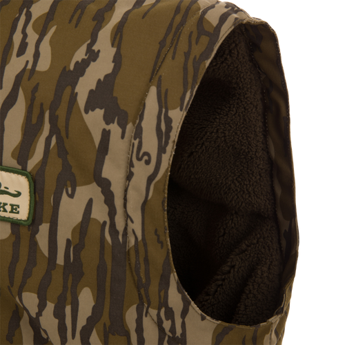 Throwback 80 Sport Vest, a sleeveless camo vest with fleece lining, features large pockets, brass zipper, and wind flap, ideal for outdoor adventures.