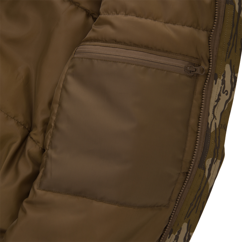 Close-up of Throwback 80 Sport 3-in-1 Jacket's interior, showcasing brown lining, internal zip-pocket, padded stitching, and edge of camo-patterned outer shell with main zipper.