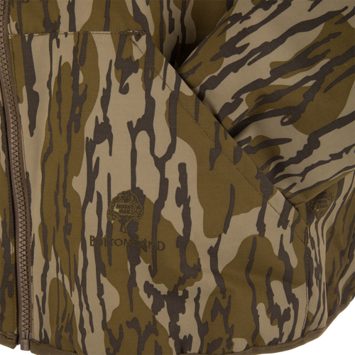 Close-up of the Throwback 80 Sport 3-in-1 Jacket in Mossy Oak Bottomland pattern, showcasing its zip closure, fold-over pocket, and detailed logo.