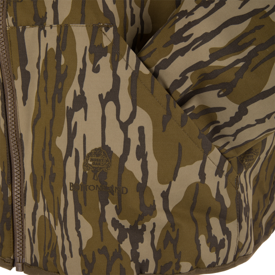 Close-up of the Throwback 80 Sport 3-in-1 Jacket in Mossy Oak Bottomland pattern, showcasing its zip closure, fold-over pocket, and detailed logo.