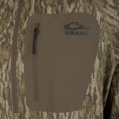 Close-up of BMF EST Offset 1.0 Quarter Zip Hoodie showing Drake Waterfowl logo on chest patch, vertical zippered pocket with pull cord, and camouflage fabric.
