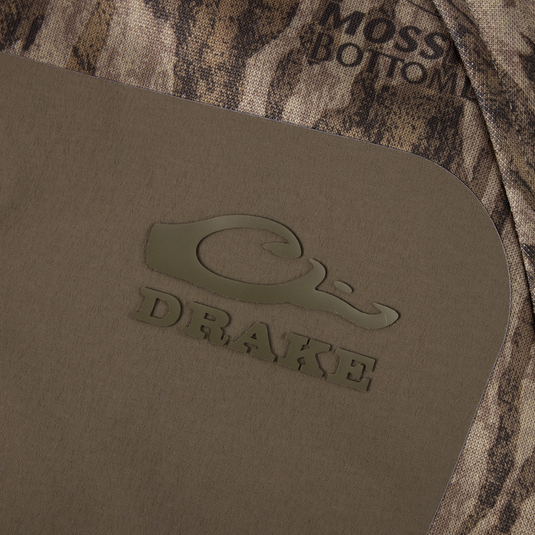 Close-up of Drake Waterfowl MST Offset 2.0 Half Zip Hoodie, featuring Mossy Bottoms camo pattern and olive-brown panel with logo, designed for comfort and functionality.
