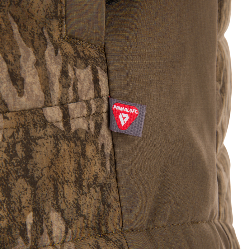 Close-up of LST BMF Jacket with Primaloft, showing a stitched tag on camouflage and olive-green fabric, highlighting its insulated, lightweight design for active use.