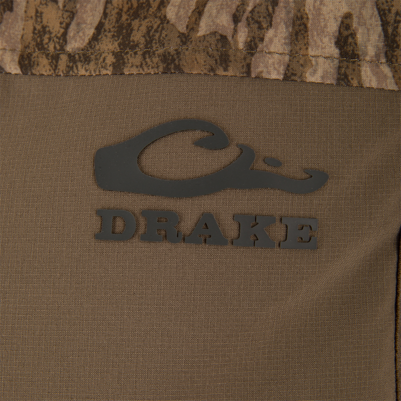Close-up of the LST BMF Vest with Primaloft, featuring the Drake Waterfowl logo on camouflage fabric, showcasing its windproof, water-resistant materials, and practical Magnattach™ pocket.