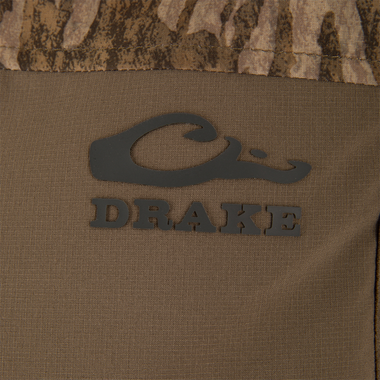 Close-up of the LST BMF Vest with Primaloft, featuring the Drake Waterfowl logo on camouflage fabric, showcasing its windproof, water-resistant materials, and practical Magnattach™ pocket.