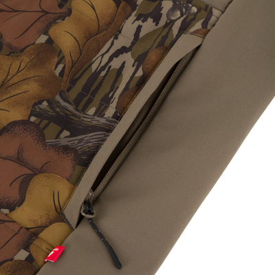 Close-up of a brown camouflage Drake X Ducks Unlimited LST BMF Vest with Primaloft featuring a zippered pocket and a small red tag on the lower seam.