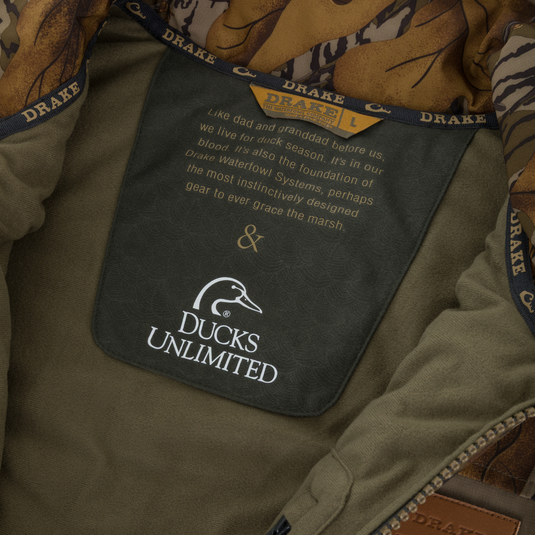 Interior tag of a camouflage-lined Drake X Ducks Unlimited LST BMF Vest with Primaloft featuring the Ducks Unlimited logo and a paragraph about waterfowl hunting heritage.