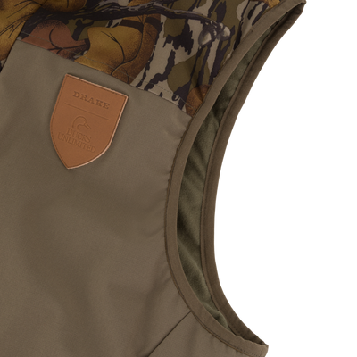 Olive green Drake X Ducks Unlimited LST BMF Vest with Primaloft featuring a camouflage shoulder panel and a leather patch embossed with a duck logo and the words Drake and Ducks Unlimited.