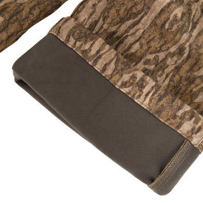 MST CommandXT Softshell Pant close-up, showing camouflage fabric with dark-grey fleece hem, highlighting flexible, windproof, water-resistant material designed for hunting and outdoor activities.