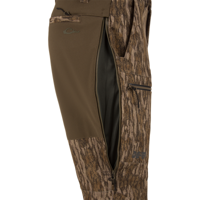 MST CommandXT Softshell Pant close-up showing camo fabric, side-zippered vent with black mesh, thigh pocket, and logo near hem for mobility and protection.