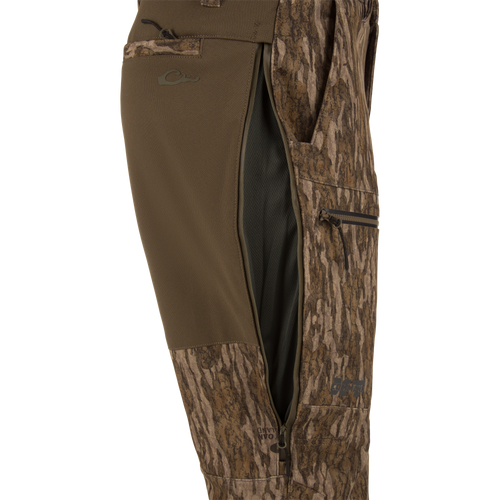 MST CommandXT Softshell Pant close-up showing camo fabric, side-zippered vent with black mesh, thigh pocket, and logo near hem for mobility and protection.