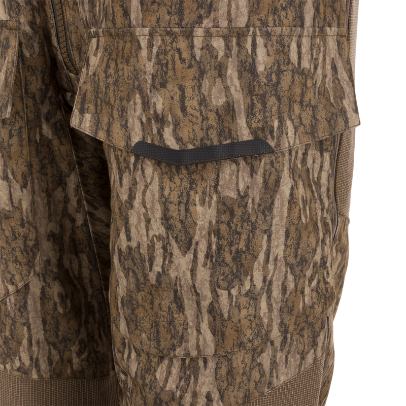 Close-up of LST CommandXT Bib with Primaloft, showcasing tree-bark camo leg with flap-covered cargo pocket and textured fabric, highlighting durability for extreme hunting conditions.