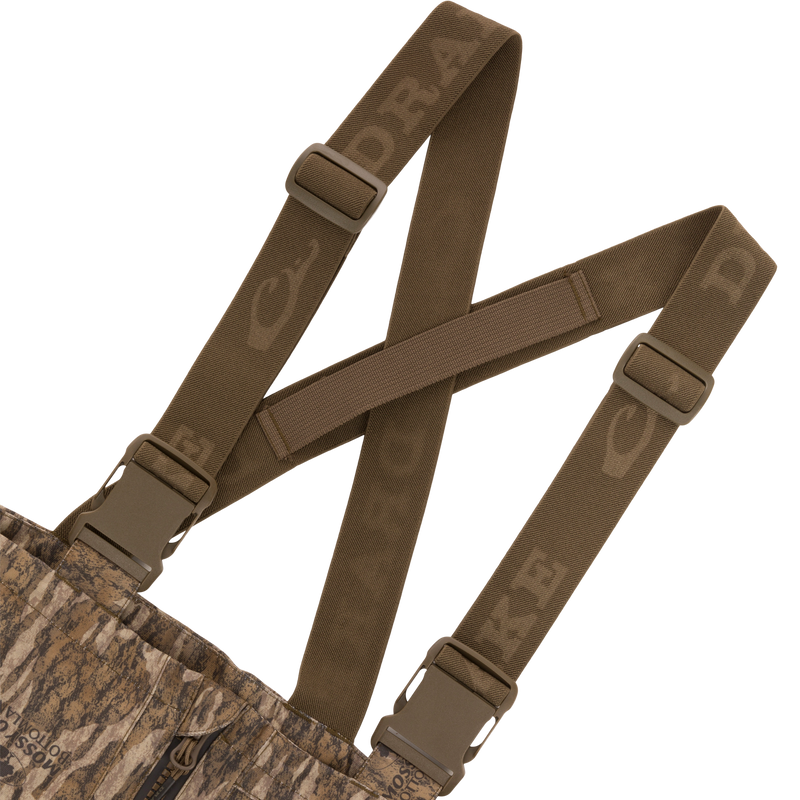LST CommandXT Bib with Primaloft shows camo pattern, X-crossed brown suspenders, side-release buckles, and Mossy Oak Bottomland logo near zipper, ideal for extreme hunting conditions.