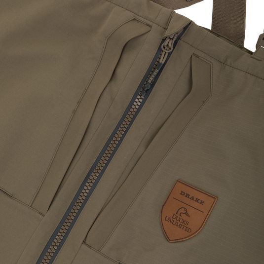 Olive green Drake X Ducks Unlimited LST BMF Pit Bib with Primaloft chest waders featuring a front zipper and a leather patch with a duck logo and Drake and Ducks Unlimited text.