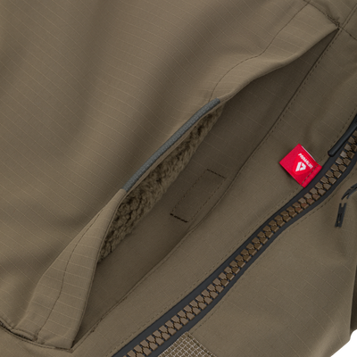 Olive green insulated pocket from a Drake X Ducks Unlimited LST BMF Pit Bib with Primaloft, featuring a fleece lining, a heavy-duty zipper, and a small red Primaloft brand tag.