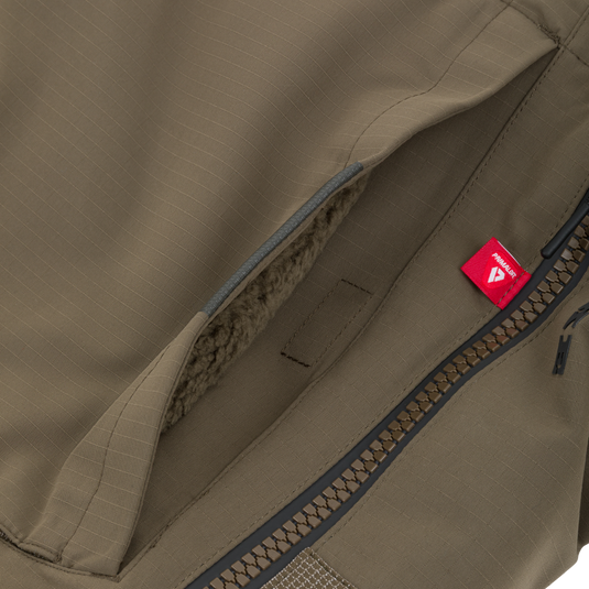 Olive green insulated pocket from a Drake X Ducks Unlimited LST BMF Pit Bib with Primaloft, featuring a fleece lining, a heavy-duty zipper, and a small red Primaloft brand tag.