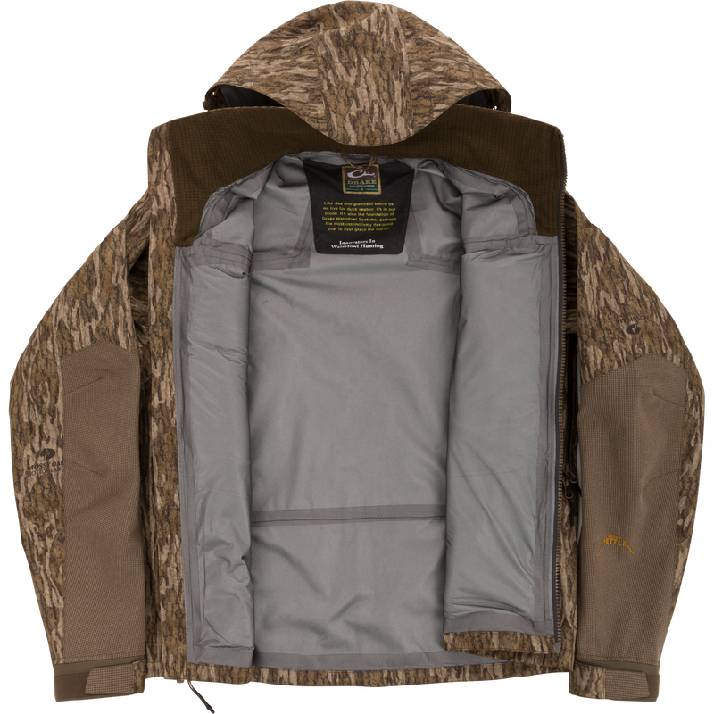 Drake Waterfowl LST BMF Pit Jacket with camo exterior, unzipped to show gray lining and label. Designed for extreme conditions with durable, weather-resistant features.