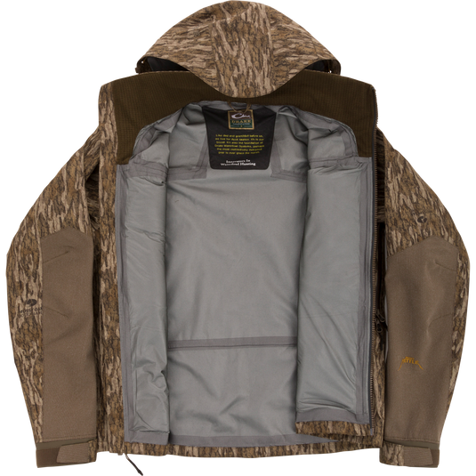 Drake Waterfowl LST BMF Pit Jacket with camo exterior, unzipped to show gray lining and label. Designed for extreme conditions with durable, weather-resistant features.