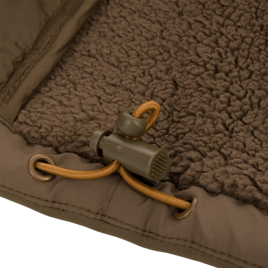 Close-up of LST BMF 3-in-1 Pit Jacket's chocolate-brown sherpa fleece lining with olive-green binding, tan drawcord, and cord-lock toggle, highlighting its rugged construction.