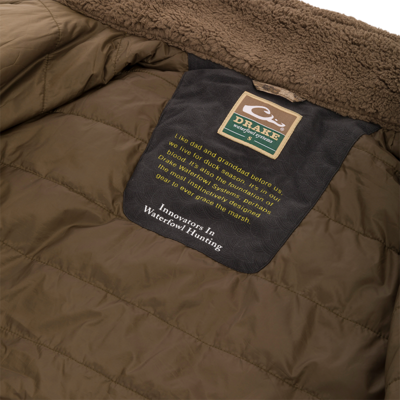 Close-up of the LST BMF 3-in-1 Pit Jacket's interior, highlighting the shearling-lined collar and Drake Waterfowl Systems label with an inspiring message about duck hunting heritage.