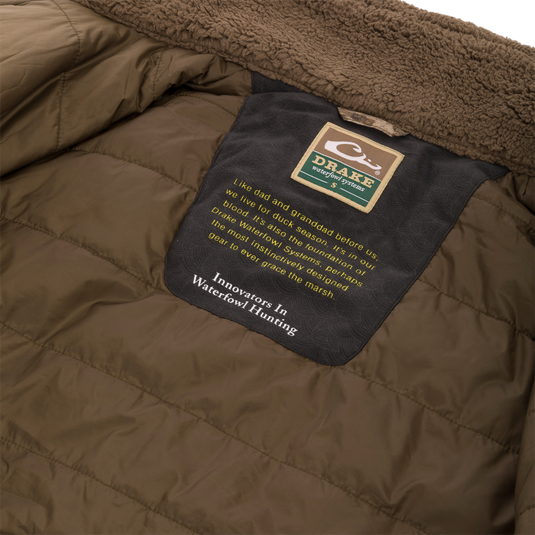 Close-up of the LST BMF 3-in-1 Pit Jacket's interior, highlighting the shearling-lined collar and Drake Waterfowl Systems label with an inspiring message about duck hunting heritage.