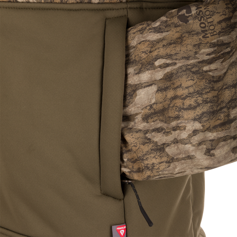LST BMF 3-in-1 Pit Jacket with Primaloft, featuring an olive-green softshell, camo-patterned sleeve, zippered pocket, and red insulation tag near the hem.