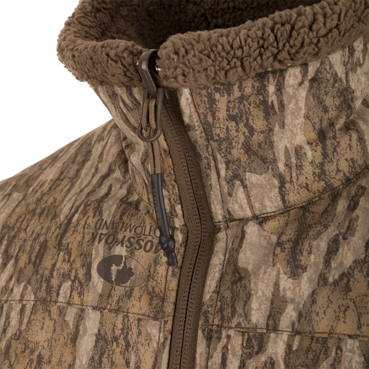 Close-up of the LST BMF 3-in-1 Pit Jacket with Primaloft, featuring Mossy Oak Bottomland camo, front zipper, and fleece-lined collar for enhanced warmth and durability.