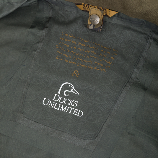Interior of a Drake X Ducks Unlimited LST BMF 3-in-1 Pit Jacket with Primaloft featuring a logo and a printed quote about the tradition of duck hunting.
