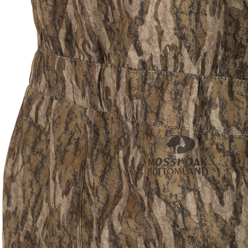 Close-up of LST Hardline Insulated Bib's camo fabric with elasticized seam and Mossy Oak logo, highlighting its durable, weatherproof design for hunting in demanding conditions.
