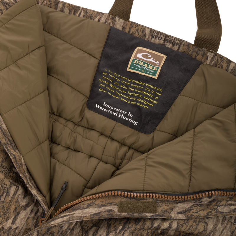 Drake Waterfowl Systems label inside the LST Hardline Insulated Bib, highlighting durable, insulated, camo-patterned construction with advanced weather protection features for waterfowl hunting.