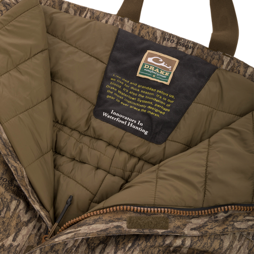 Drake Waterfowl Systems label inside the LST Hardline Insulated Bib, highlighting durable, insulated, camo-patterned construction with advanced weather protection features for waterfowl hunting.