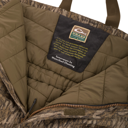 Drake Waterfowl Systems label inside the LST Hardline Insulated Bib, highlighting durable, insulated, camo-patterned construction with advanced weather protection features for waterfowl hunting.