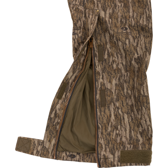 LST Hardline Insulated Bib in Mossy Oak Bottomland camo, showing Velcro straps and olive-green lining. Designed for harsh hunting conditions with superior warmth and protection.