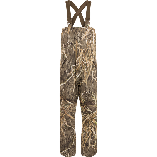 LST Hardline Insulated Bib: Camouflage overalls with adjustable straps, durable waterproof polyester, insulated for warmth, featuring handwarmer pockets, storm flaps, and articulated knees for hunting.