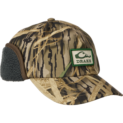 MST Flap Cap with camo pattern and DRAKE patch, features fold-down fleece ear flaps for warmth, ideal for cold-weather outdoor activities.