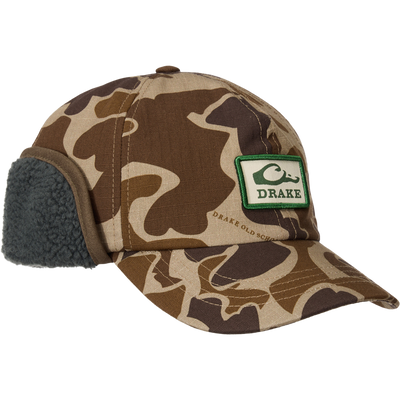MST Flap Cap with camo pattern features fold-down sherpa-lined ear flaps, a Drake patch, and adjustable clasp for cold-weather outdoor use.