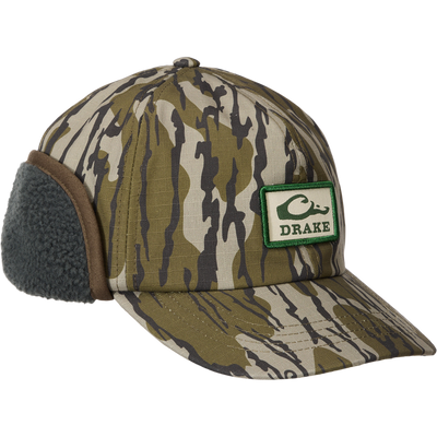 MST Flap Cap: Camouflage hunting cap with fleece-lined ear flaps, adjustable clasp, and DRAKE patch, designed for warmth and durability in cold weather.