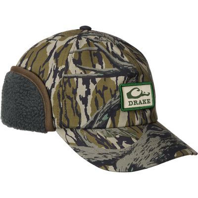 MST Flap Cap featuring a camo pattern, fleece earflaps, and DRAKE logo, designed for warmth and durability in cold-weather hunting conditions.