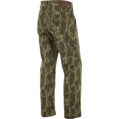 Throwback80 Field Pant on mannequin: camo-patterned, loose-fit cargo with brass buttoned side pocket, reinforced back pockets, and double-layer knee, embodying rugged, durable hunting style.