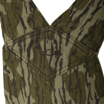 Close-up of Throwback80 Field Bib's olive-green camouflage fabric showing heavy twill weave, triangular panel seams, and embroidered logo, emphasizing rugged durability for hunting and workwear.
