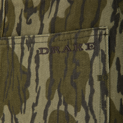 Close-up of Throwback 80 Field Bib, showcasing camouflage fabric, folded seam, visible pocket edge with embroidered lettering, embodying durable, heritage-inspired workwear.