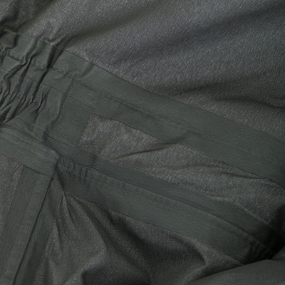 Close-up of BMF Uninsulated Pit Bib's dark green elastic waistband, detailed pocket stitching, and ripstop texture, highlighting its durable, flexible, waterproof fabric.