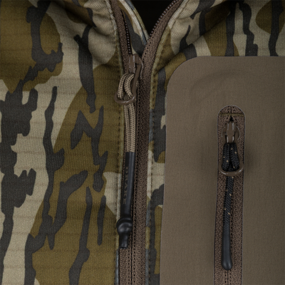 Close-up of Drake Waterfowl's Grid Fleece Half Zip Hoodie, highlighting camo fabric, main zipper with corded pull, and water-resistant chest pocket with branded pull.
