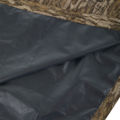 RTL - El Poncho: Close-up of Mossy Oak Bottomland camo fabric on a waterproof poncho, featuring snap-fasteners, ideal for hunting and outdoor protection against elements.