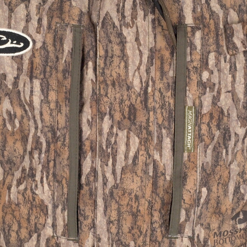 A close-up of the LST Insulated Bib 2.0, featuring a camouflage jacket with fleece-lined hand warmer pockets and full-length zippers on each side.