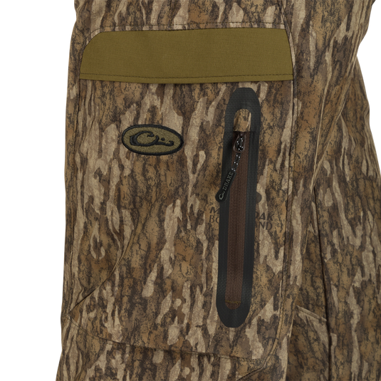 A close-up of the Women's EST Camo Stretch Tech Pants, featuring a camouflage jacket, bag, zipper, logo, fabric, and more. Made from lightweight polyester, these pants offer breathability and comfort for any hunting activity. Adjustable waistband, multiple pockets, and elastic ankle cinch cord provide convenience and functionality. Perfect for big game hunting, waterfowl hunting, turkey hunting, and fishing.