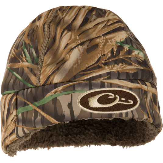 Camouflage-patterned Drake LST Windstopper Beanie with embroidered logo, featuring fleece lining and windproof membrane, designed to cover ears for warmth and comfort during waterfowl hunting.