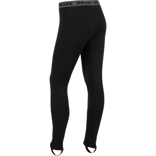 LST Heavyweight Baselayer Pant: A person's legs in black tights wearing a black pants with a grey band. Ideal for active and cold weather activities. Exceptional stretch, extreme warmth, and moisture-wicking properties. Stirrup strap for layering under waders and front fly for convenience. Stay warm and comfortable in any condition.