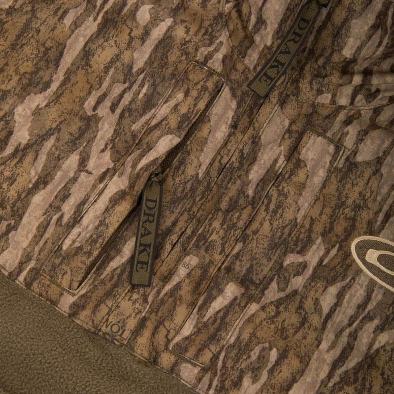 Close-up of the MST Youth Eqwader Quarter Zip Jacket, showcasing camouflage pattern, multiple zip-up pockets, and “DRAKE” branded zipper pulls, transitioning to a solid brown fleece.