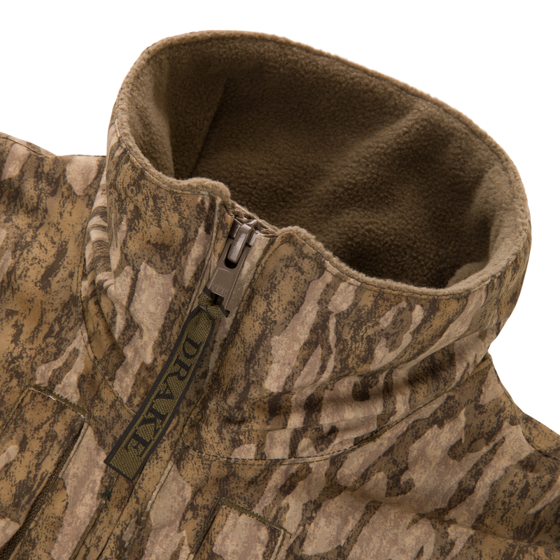 Close-up of the MST Youth Eqwader Quarter Zip Jacket, featuring a camouflaged, fleece-lined design with a tall collar, branded DRAKE zipper pull, and patented waterproof technology.